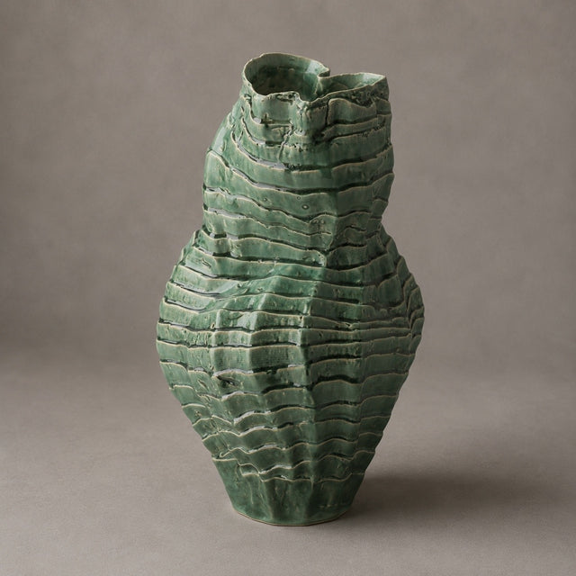 A textured green ceramic vase with a ribbed, layered surface pattern, photographed against a neutral gray studio background.