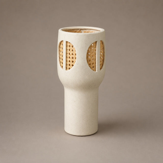 A modern ceramic vase with a textured off-white body and two oval cutouts on the front filled with woven natural cane, set against a solid taupe background.