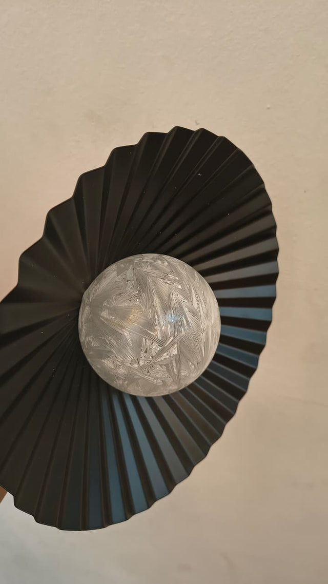 Decorative black fan with a silver ball in the center on a beige background