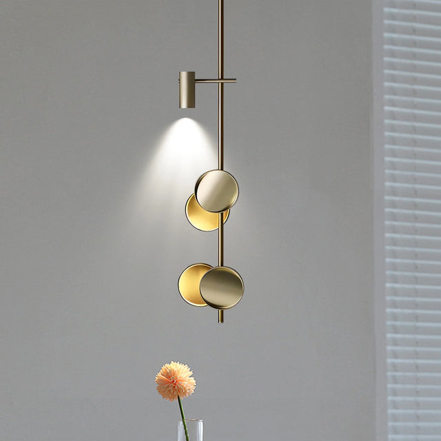 Modern gold pendant light fixture on a gray wall with a flower vase in the foreground.