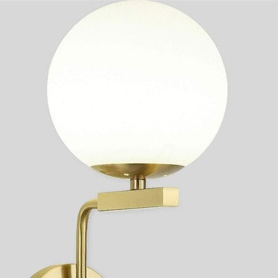 Modern wall lamp with gold fixture and white globe on a gray background