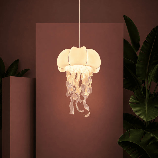 Jellyfish-shaped lamp hanging against a pink wall with plants around