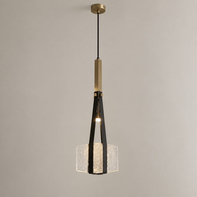 A modern pendant light fixture with a brushed brass top canopy and central rod, a black metal frame, and a textured clear glass shade, shown hanging against a plain light gray wall.