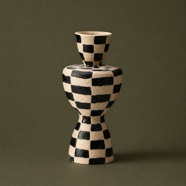 A ceramic vase with a textured black and cream checkerboard pattern, set against a solid dark olive green background.