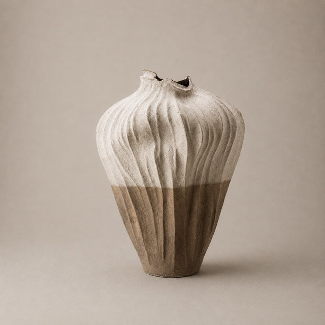A handmade ceramic vase with a textured, ribbed design, featuring a two-tone color palette of off-white on the upper half and a warm taupe-brown on the lower half, set against a solid neutral beige background.