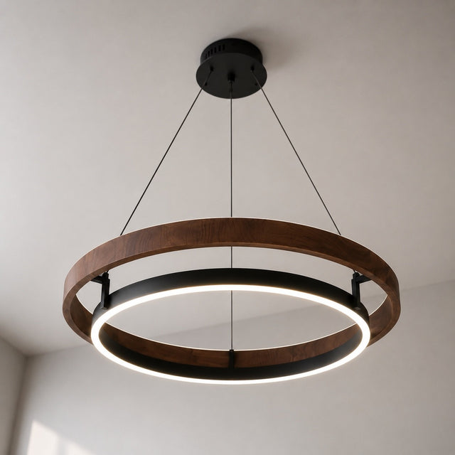 A modern double-ring LED pendant light with a dark brown wood frame and black metal accents, suspended from a ceiling in a minimalist room.