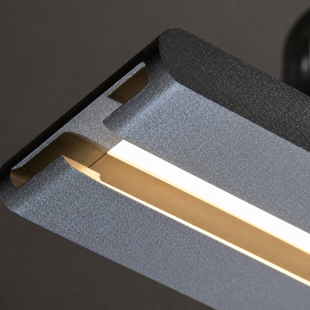 Close-up of a modern linear LED light fixture with a textured dark gray metal housing and a glowing warm white light strip.