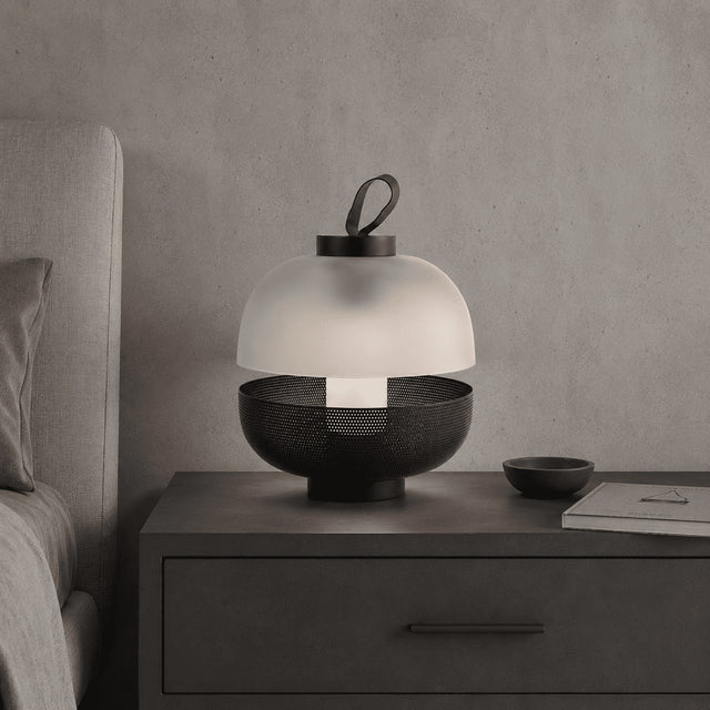 Modern table lamp with a white shade and black base on a nightstand next to a bed.