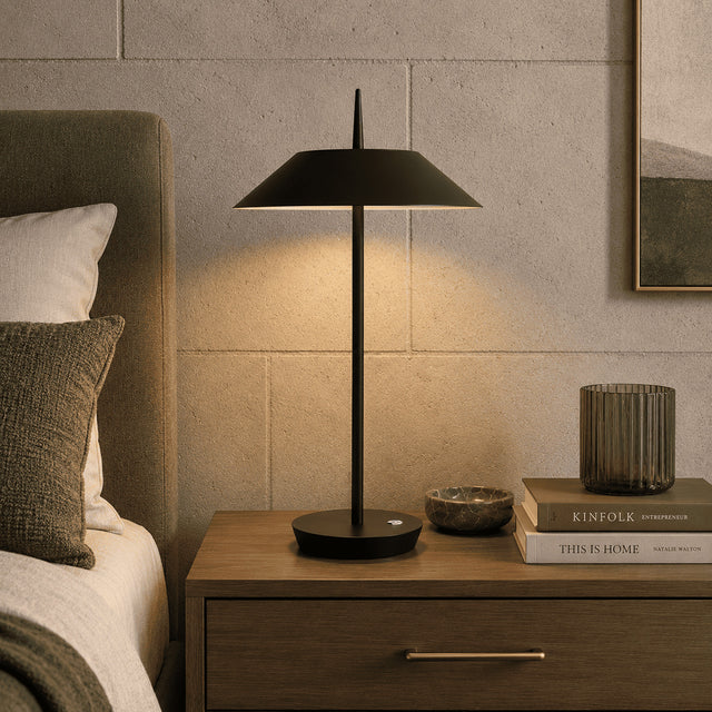 Modern black table lamp on a wooden nightstand next to a bed with books and decor items.