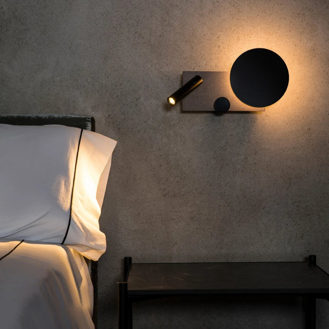 Modern wall sconce on a textured wall above a bed in a bedroom setting.