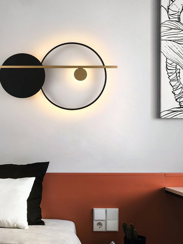 Modern wall light fixture on a white wall above a bed with black and white pillows.