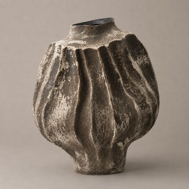 A textured ceramic vase with a ribbed, bulbous shape and a narrow neck, featuring a distressed charcoal gray and white glaze, set against a solid warm gray background.