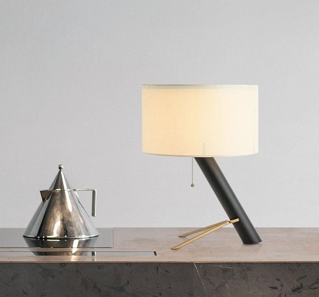Modern table lamp with a white shade on a wooden surface against a gray wall.