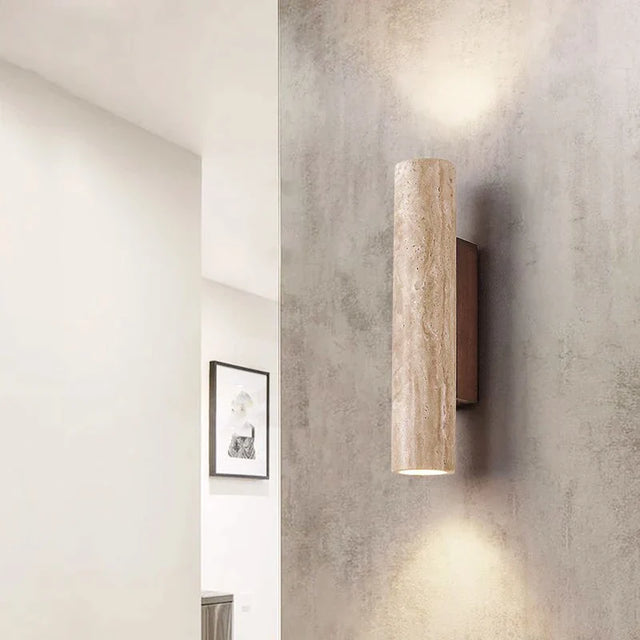 Cylindrical wall light fixture on a textured wall with a neutral color scheme.
