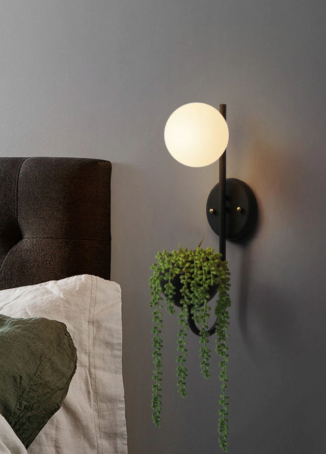 Wall-mounted light fixture with a plant on a gray wall next to a bed.