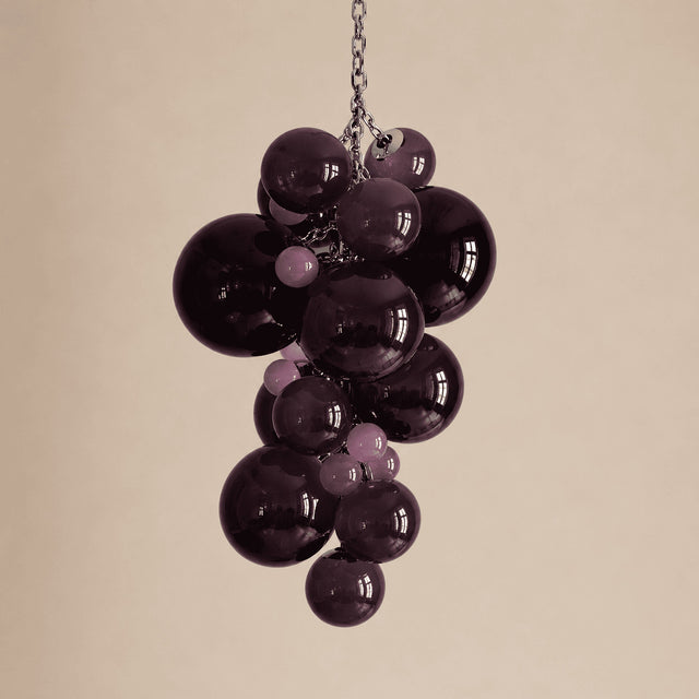 Bunch of purple grapes hanging from a chain on a beige background