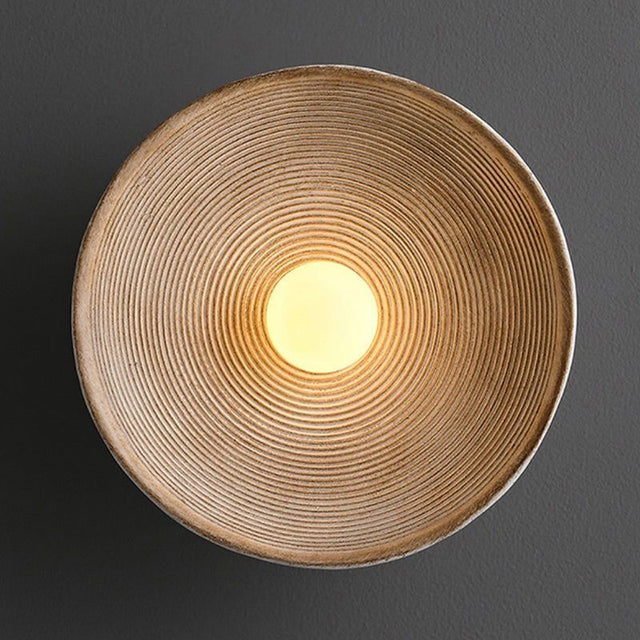 Round wall light fixture with textured design on a dark background