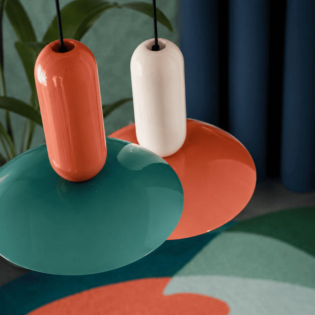 Two ceramic vases, one orange and one white, on a colorful surface with a blurred background.